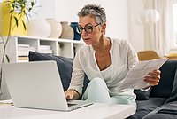 Frau arbeitet am Laptop mit Unterlagen in der Hand