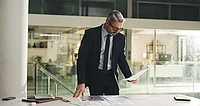 Prüfer im Anzug kontrolliert im Büro konzentriert Unterlagen bei einer Betriebsprüfung