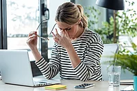 Gestresste Büroangestellte macht eine Pause vom Laptop – Belastung durch Mehrfachbeschäftigung