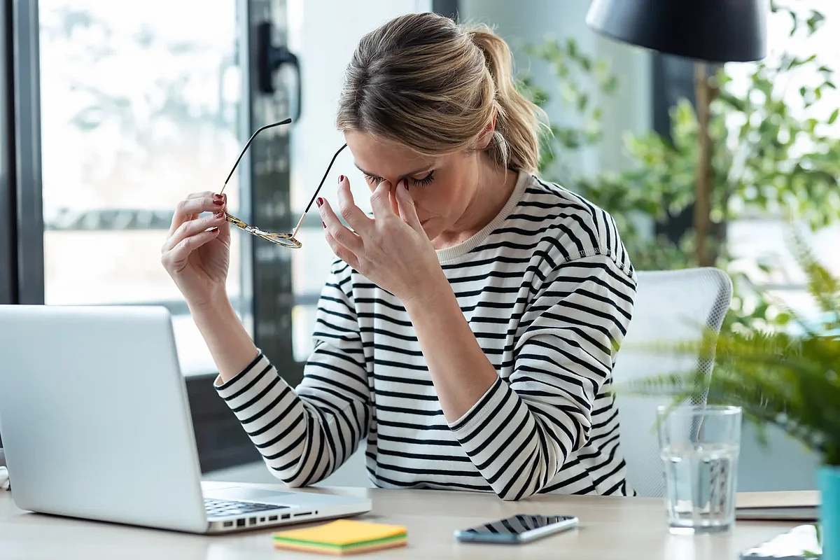Gestresste Büroangestellte macht eine Pause vom Laptop – Belastung durch Mehrfachbeschäftigung