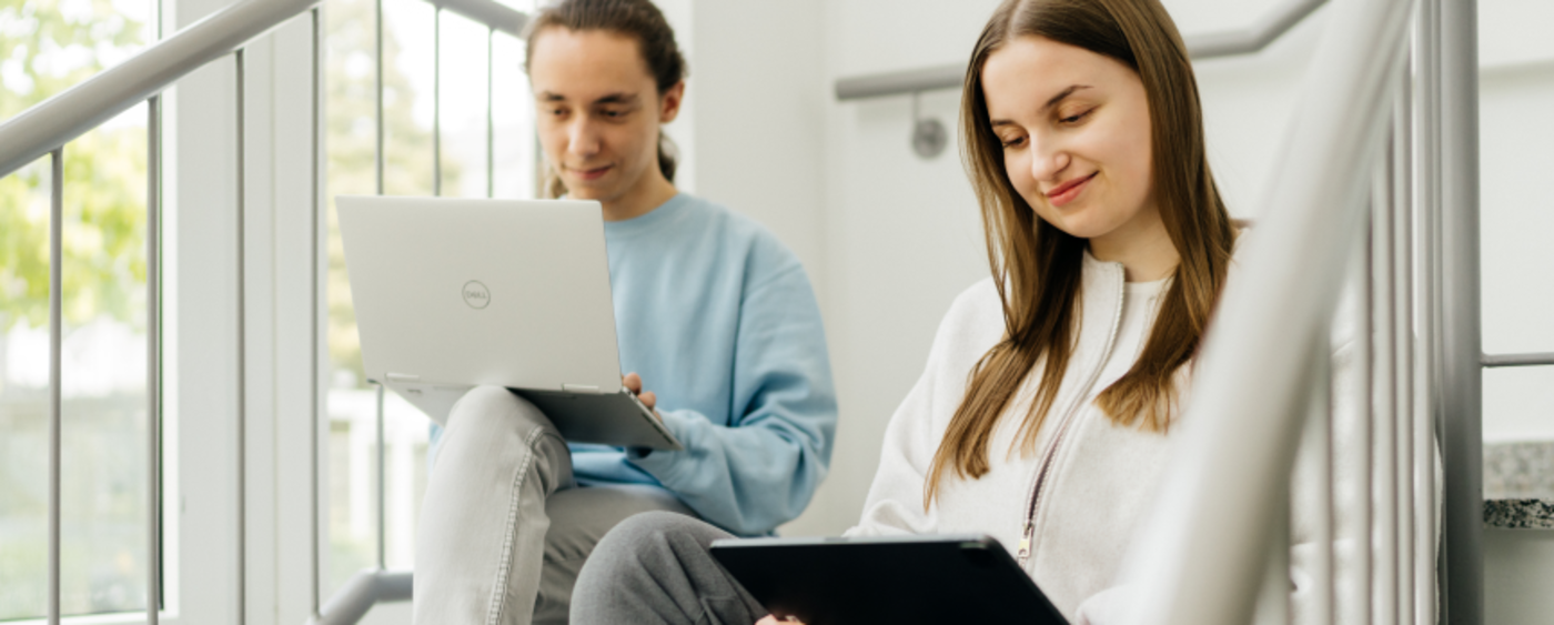 Zwei Schüler sitzen mit Laptop und iPad auf einer Treppe