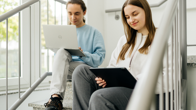 Zwei Schüler sitzen mit Laptop und iPad auf einer Treppe