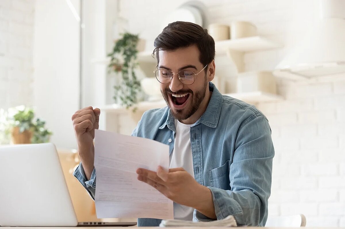 Ein Arbeitnehmer hält seine Gehaltsabrechnung in der Hand und ballt dabei die Faust vor Freude