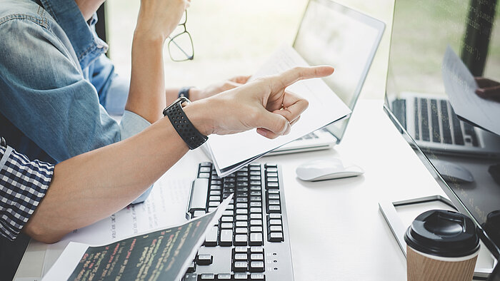 Programmierer arbeiten zusammen an einem Projekt und betrachten Code auf einem Computerbildschirm, während eine Person auf den Bildschirm zeigt.