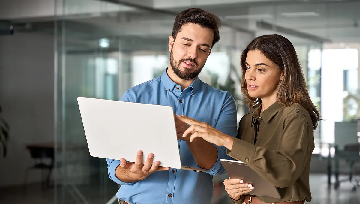 Zwei Mitarbeitende vergleichen Zeiterfassungs-Software 2026 auf Laptop und Tablet im modernen Büro