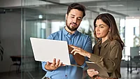 Zwei Mitarbeitende vergleichen Zeiterfassungs-Software 2026 auf Laptop und Tablet im modernen Büro