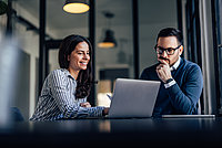 Zwei Personen schauen sich was auf dem Laptop an und überlegen